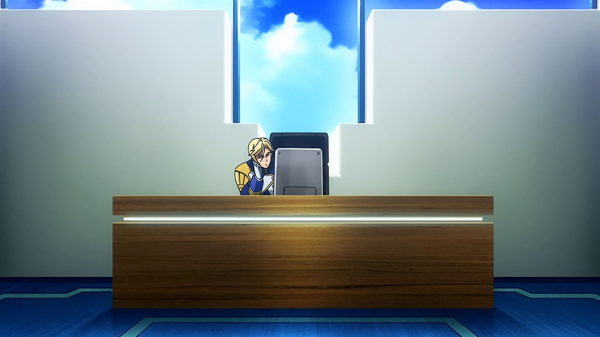 McGillis sitting at a desk, he looks annoyed.