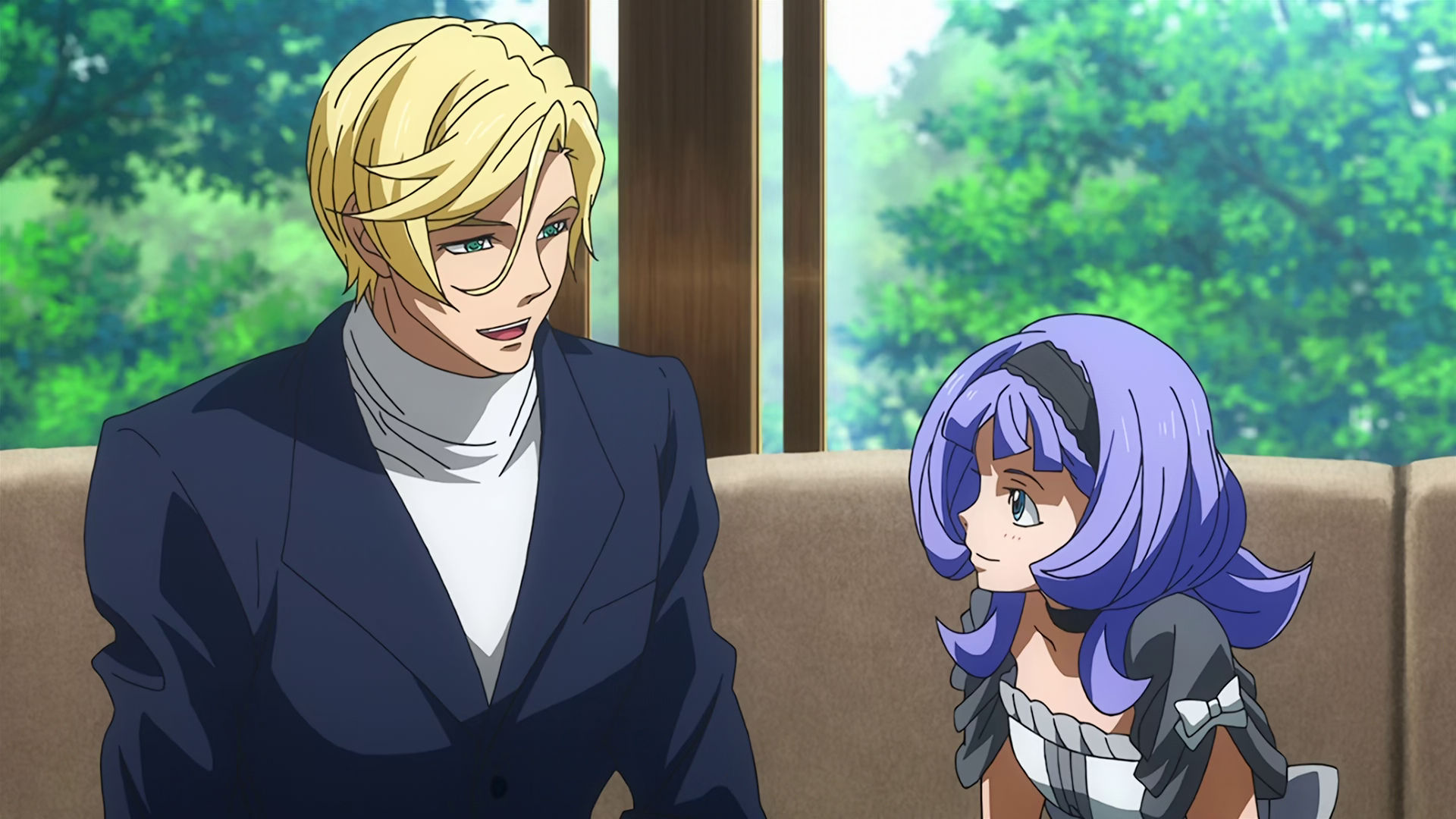 McGillis wearing a black suit and white turtleneck happily talking to Almiria.