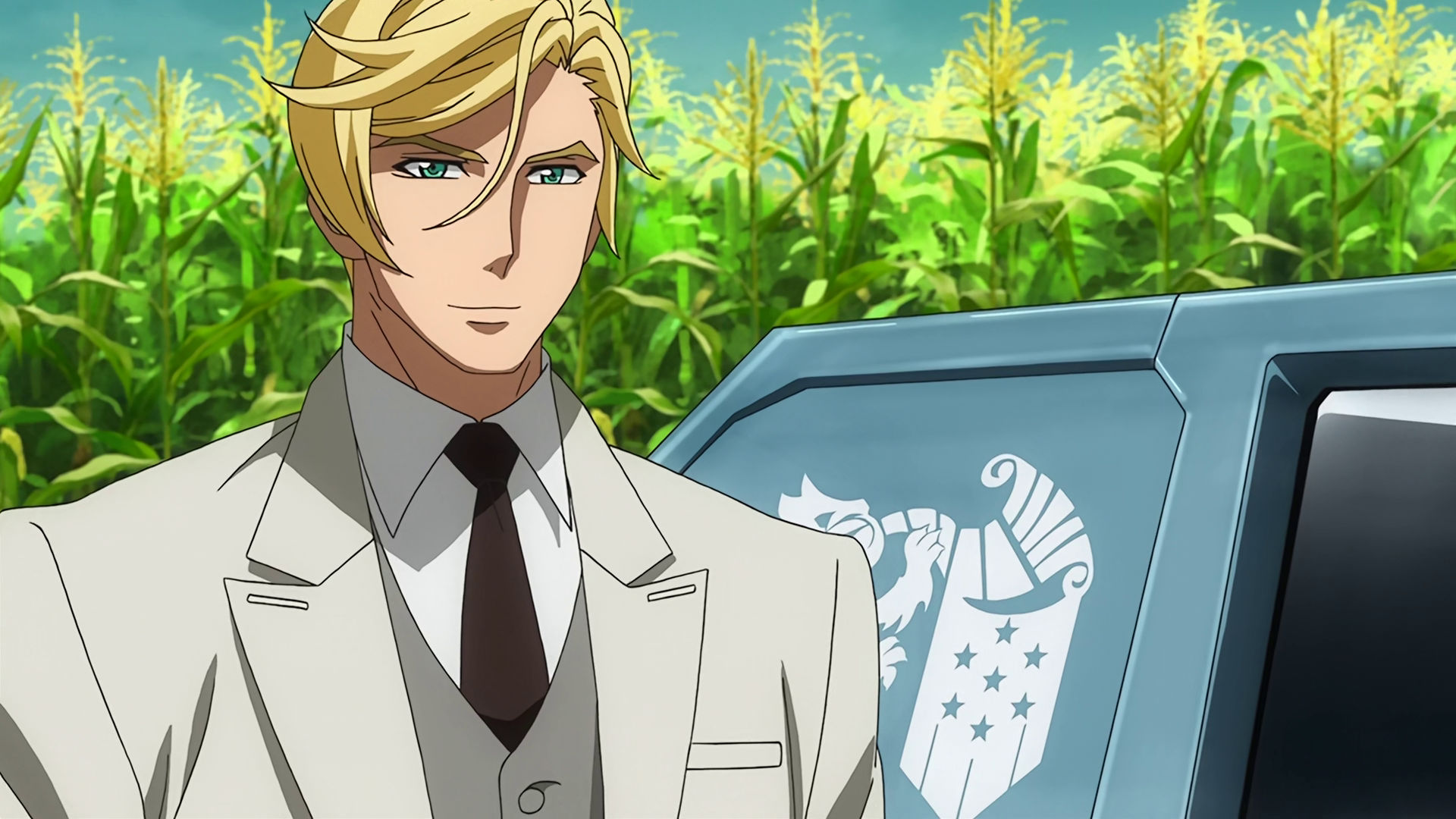 McGillis wearing an off-white suit standing in front of a cyan Gjallarhorn car and a cornfield, he is smiling.  